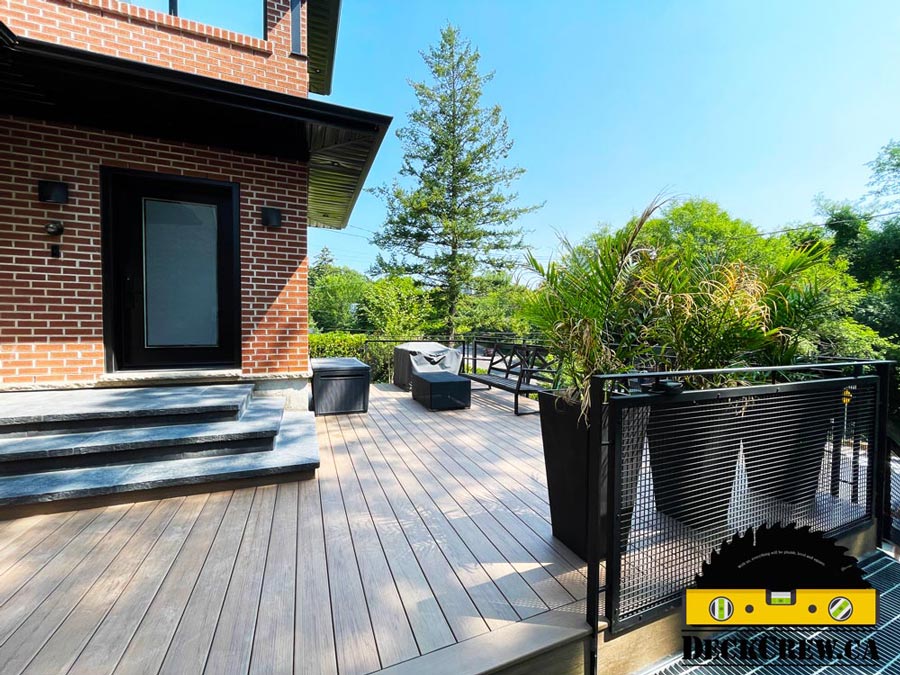 Composite deck in High Park with wide steps, black metal railings and large planters beside a brick house.