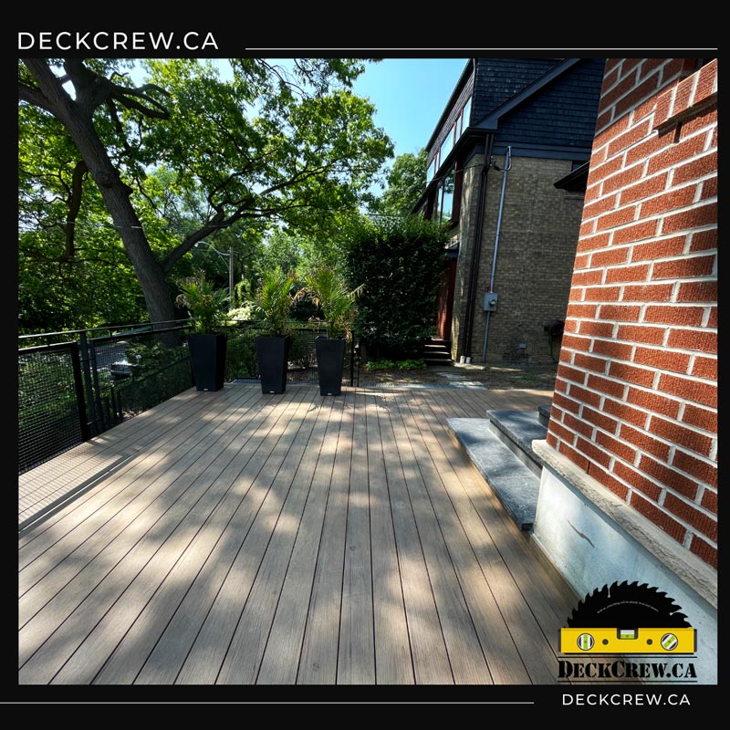 Spacious composite deck in High Park with woodgrain boards, black mesh railings and three tall planters beside a brick house.