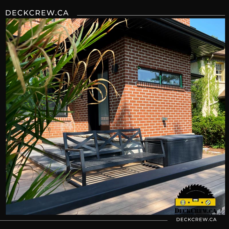 Composite deck in High Park with a black garden bench, outdoor storage box and wide steps beside a red brick house.