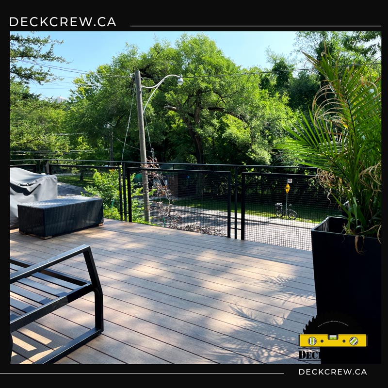 Composite deck in High Park with black metal mesh railings, outdoor seating and a tall planter overlooking a tree-lined street.