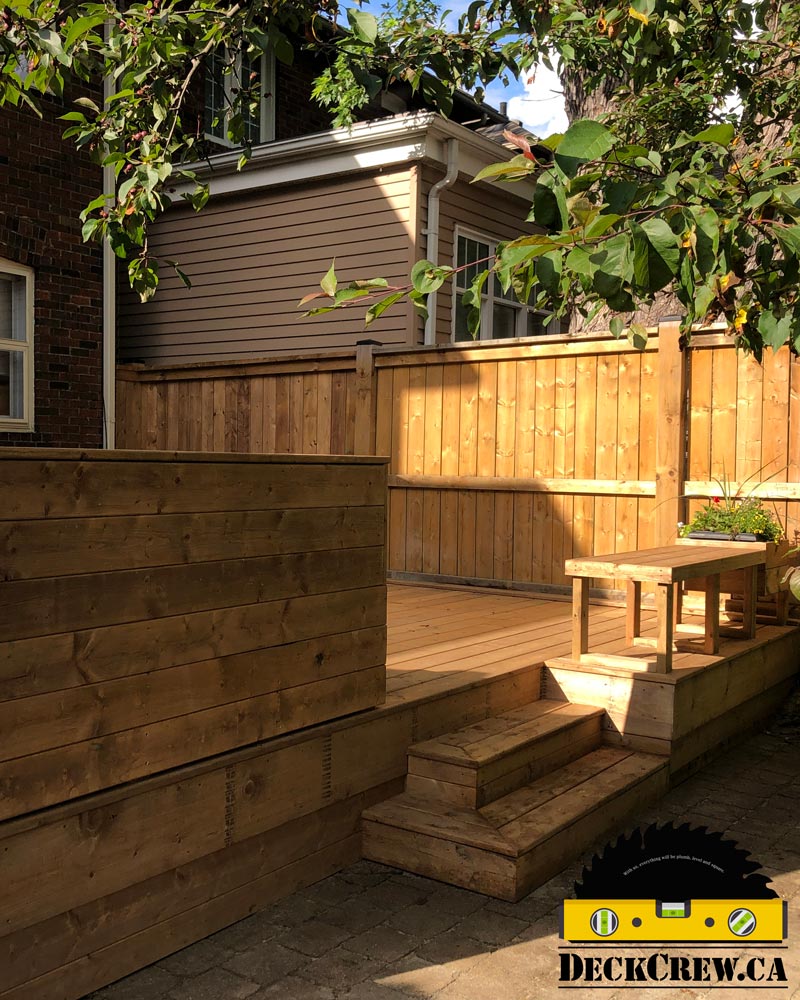 Pressure-treated deck in Bloor West Village with wood steps, built-in seating, a planter and tall privacy screens.