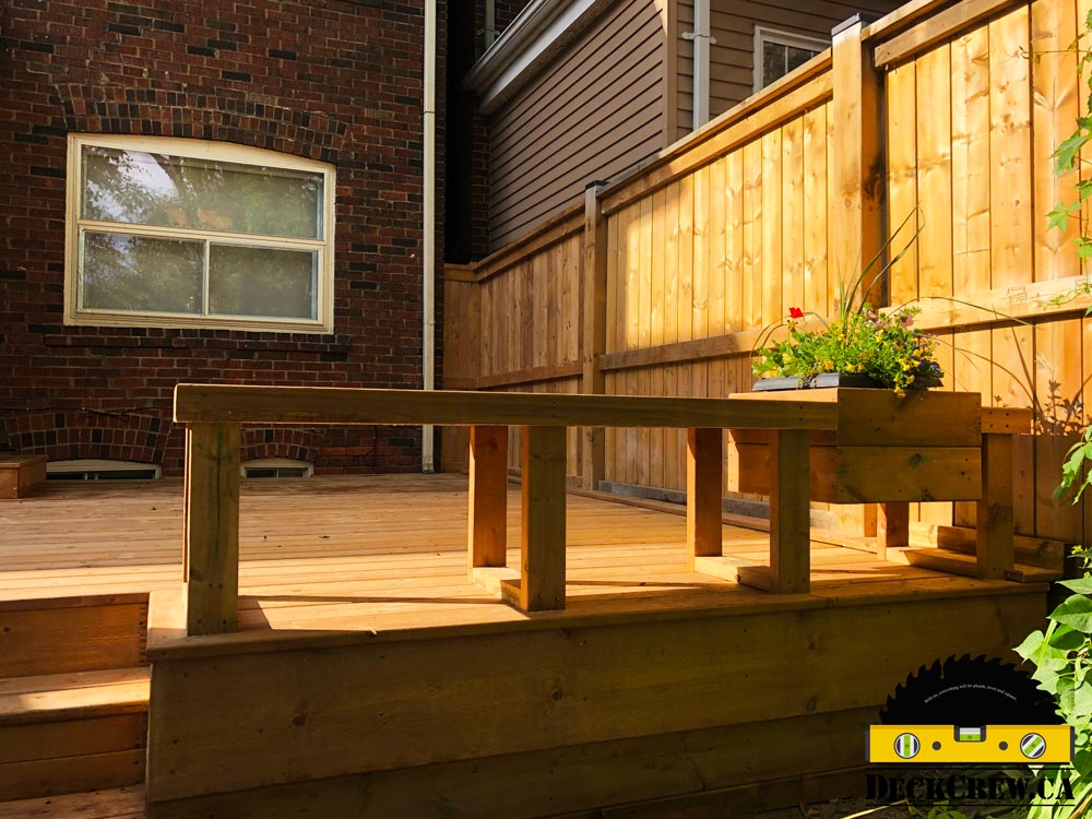 Pressure-treated deck in Bloor West Village with an open wood bench, flower planter, privacy screen and matching skirting.